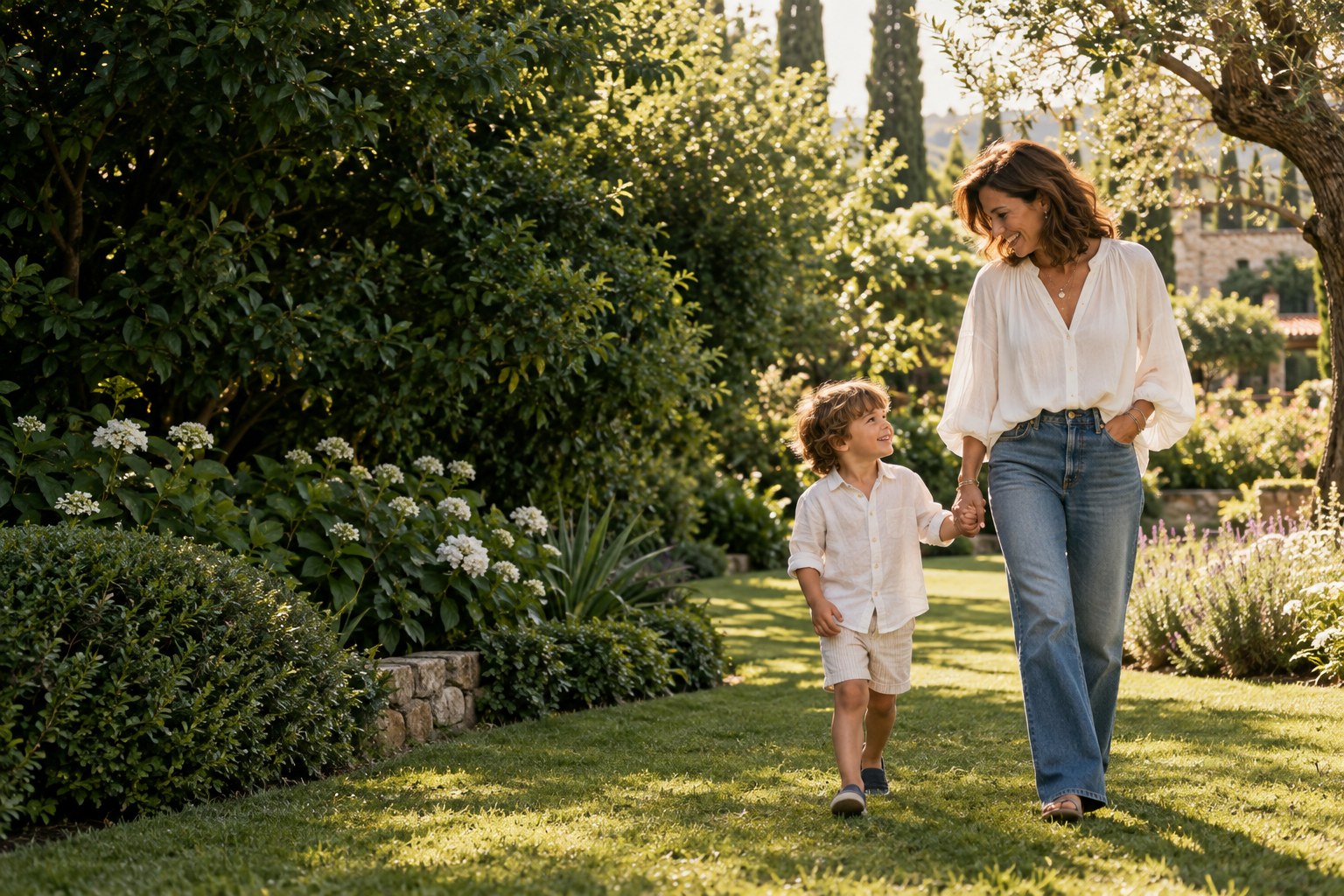 A grandmother and her young grandson walking hand in hand through a sunlit garden
